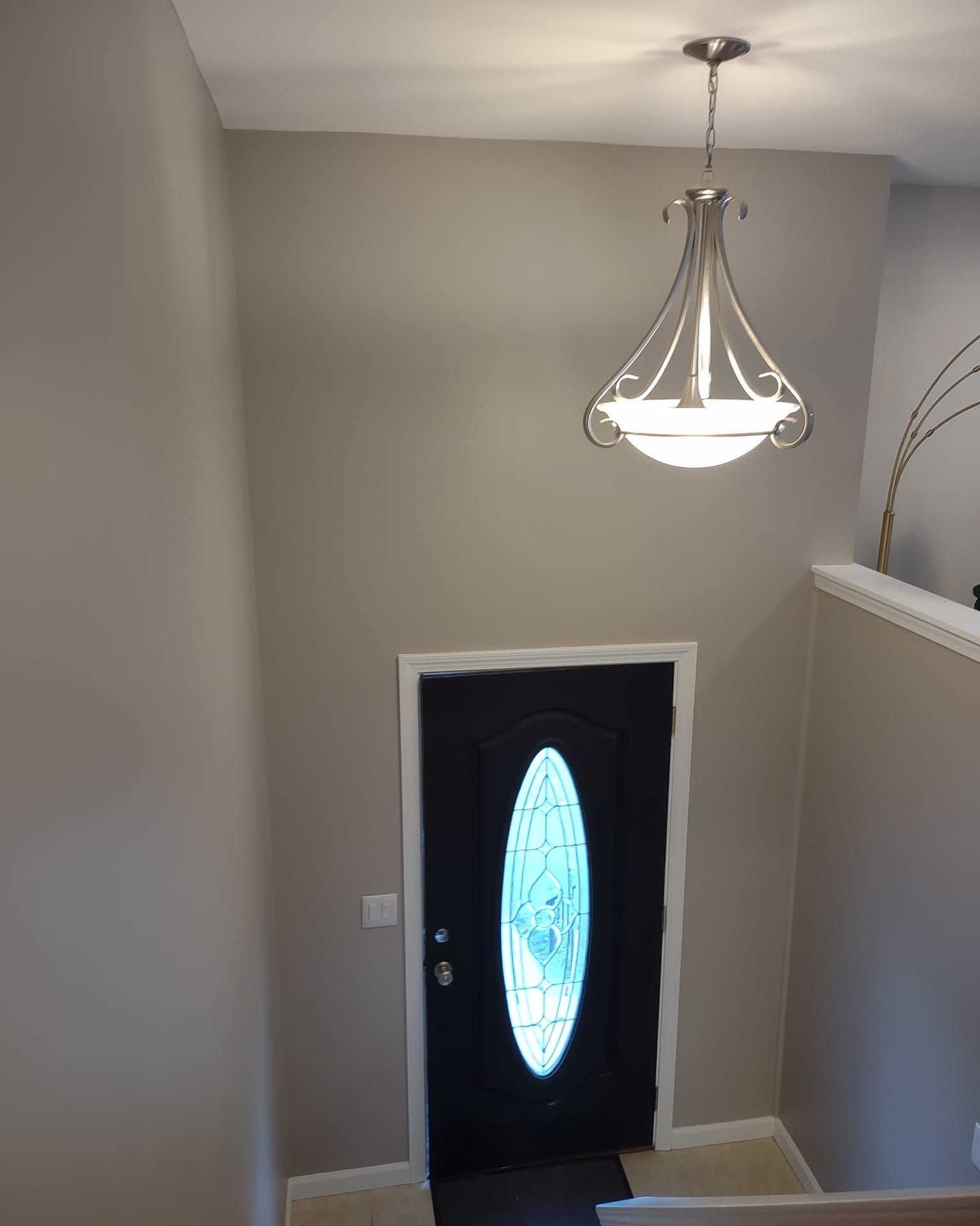 Stairwell with beige walls and a black front door with an oval frosted glass insert under a pendant light