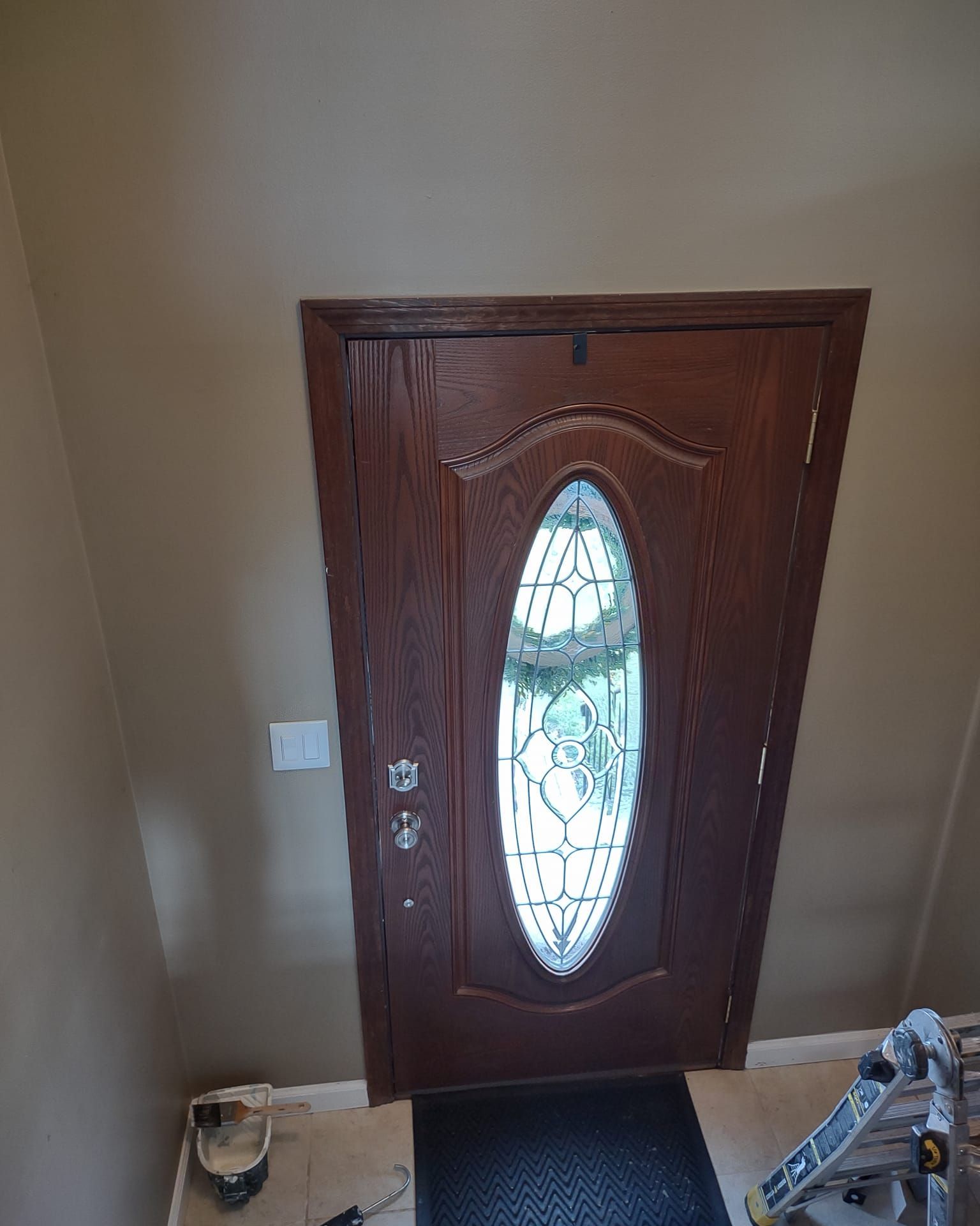Front door with oval stained-glass window and dark wood finish in a beige entryway