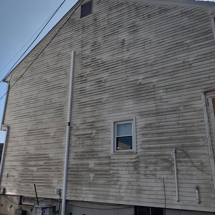 Side of weathered gray house with a small window and metal downspout