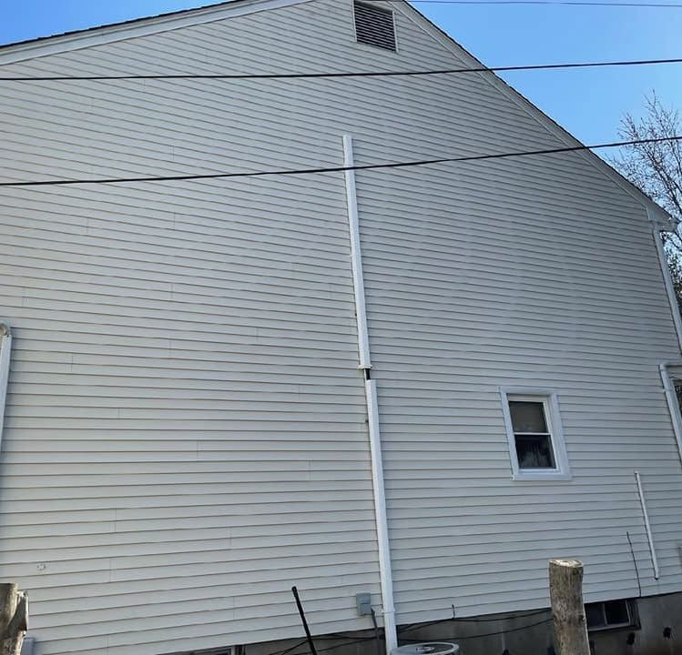 Side of a gray house with white trim, a small window, and utility pipes