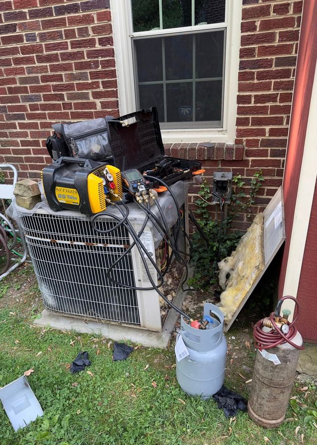 Outdoor HVAC unit beside a brick house, cluttered with tools, a gas can, and debris in the yard.