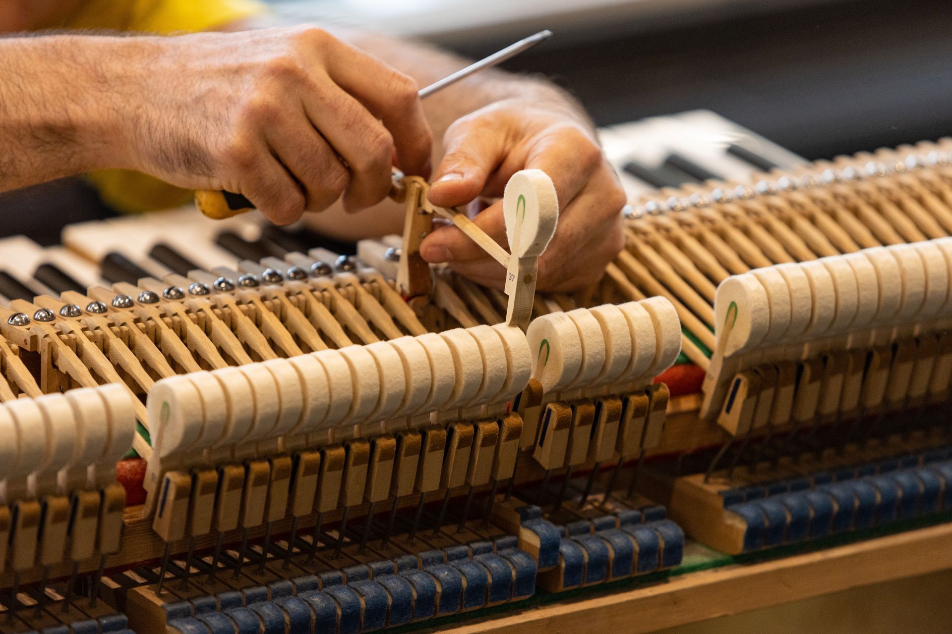 Hands adjusting piano hammers and strings inside a wooden upright piano.