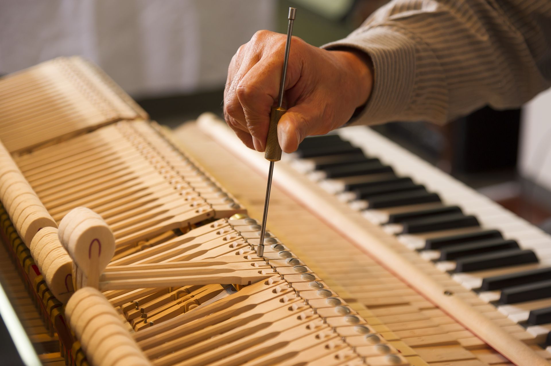 Hands tuning a piano with a tuning fork and tool over exposed strings and keys