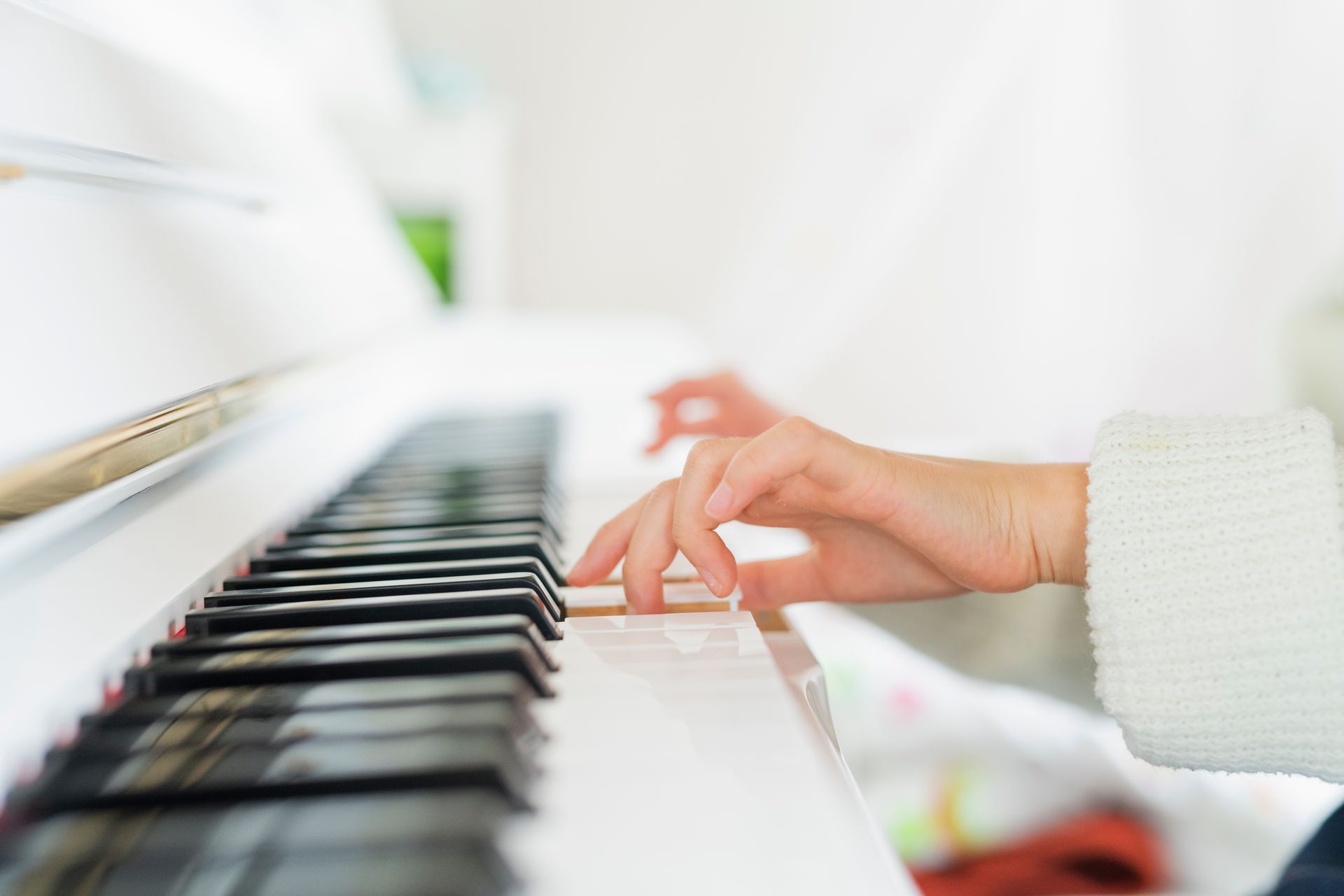 Hands playing a white piano keyboard in a bright, softly lit room