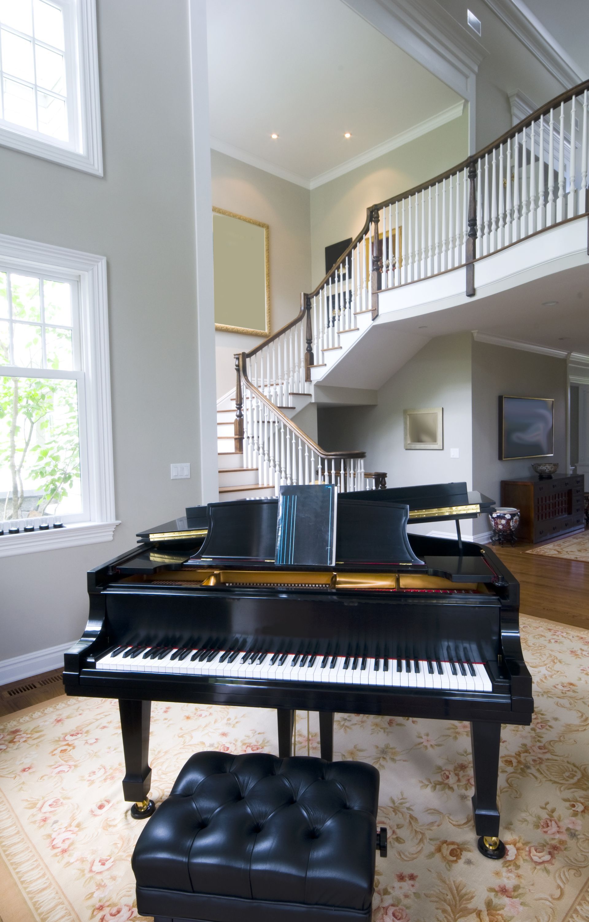 Black grand piano in a bright living room with a staircase and tall windows