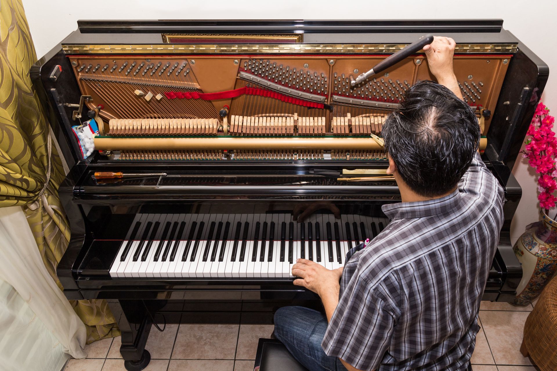 Technician adjusts the strings inside an upright piano with the front panel removed.