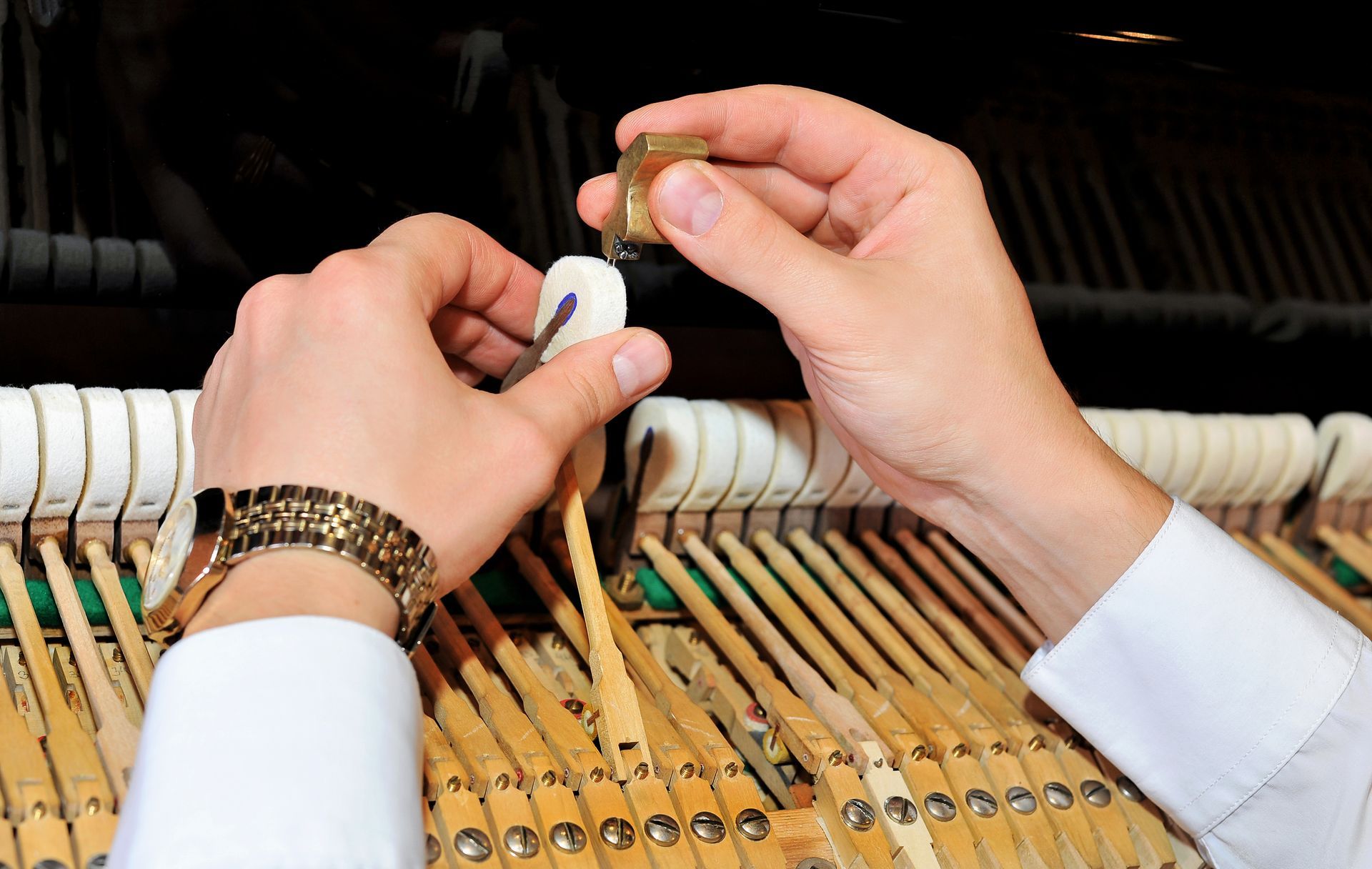 Hands tuning piano strings inside an upright piano with a tuning tool