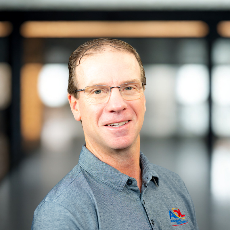 Smiling man in glasses and blue polo shirt against a blurred indoor background