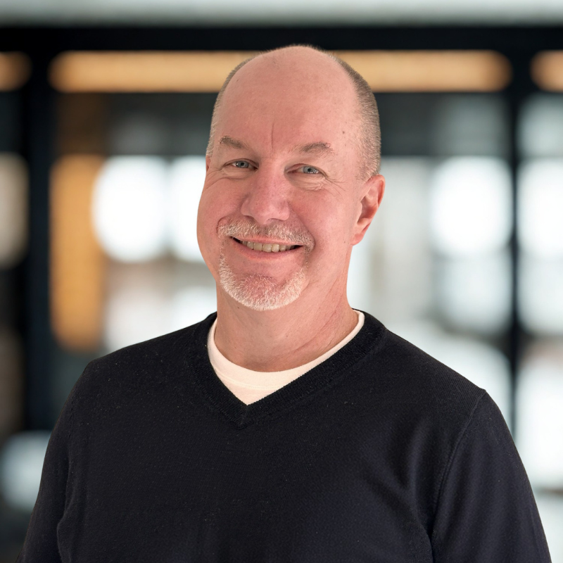 Smiling bald man in a black sweater against a blurred indoor background