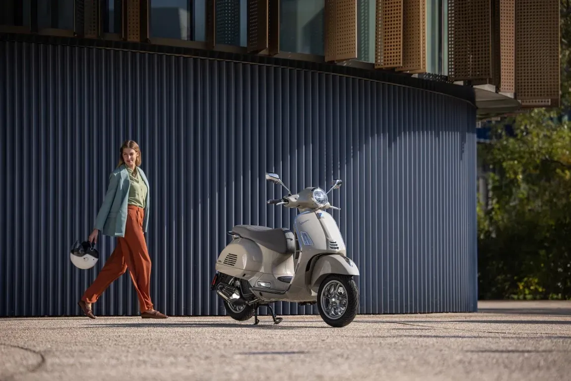 Eine Person geht auf einen beigefarbenen Vespa-Roller zu