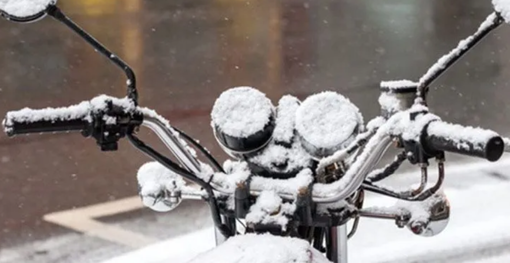 Der Lenker und das Instrumentenbrett eines Motorrads sind mit einer dicken Schicht Neuschnee bedeckt
