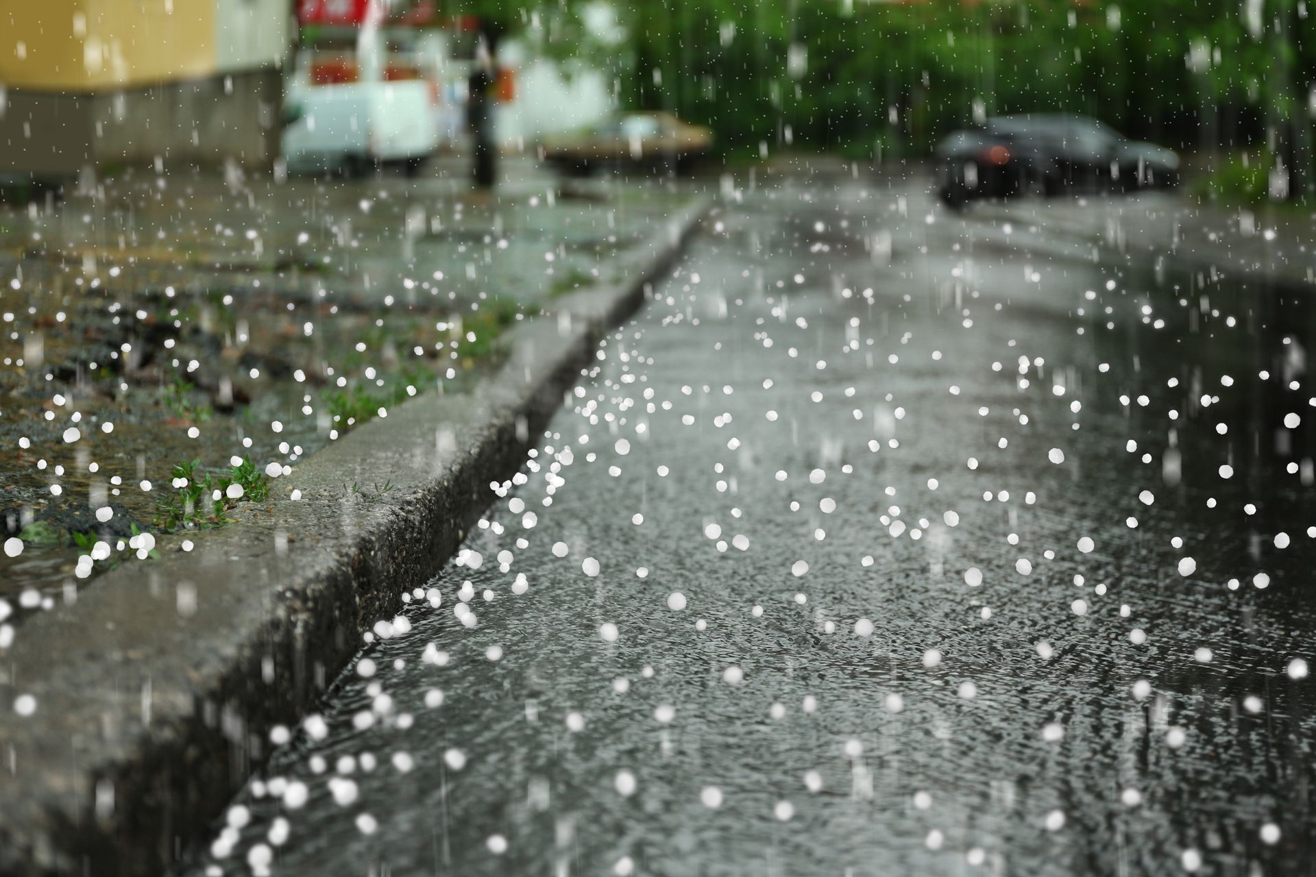 Während eines Sturms fallen Hagelkörner auf eine nasse Asphaltstraße und den Bordstein.