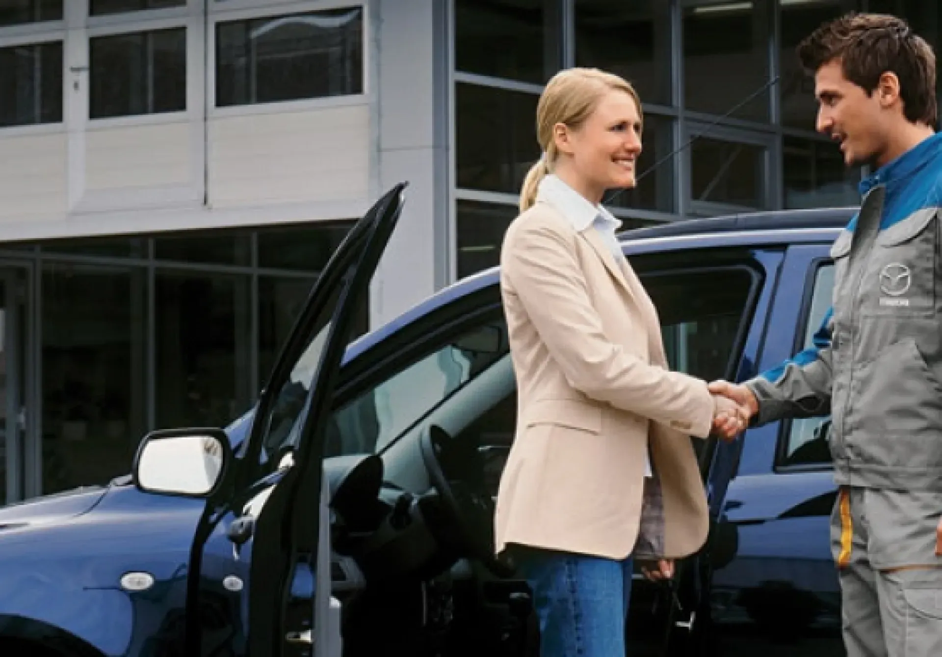 Eine lächelnde Person in einem beigen Blazer schüttelt einem Techniker in grauer Uniform die Hand.