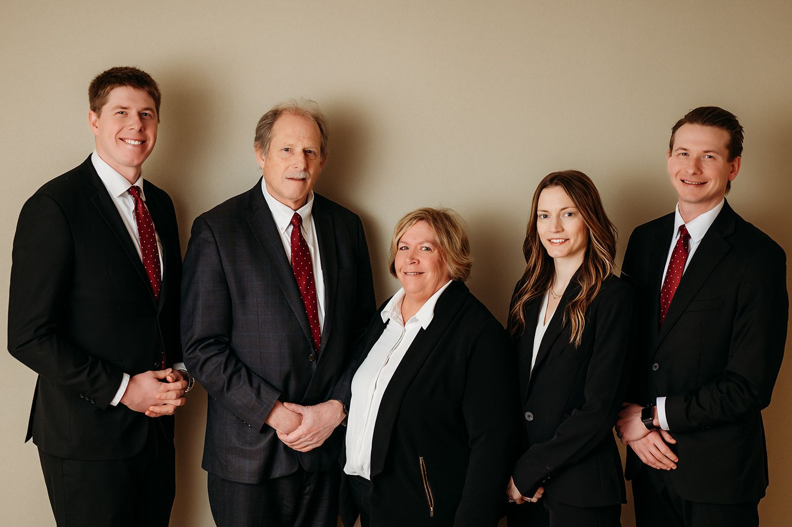 Six people in formal attire pose for a group photo against a neutral background.