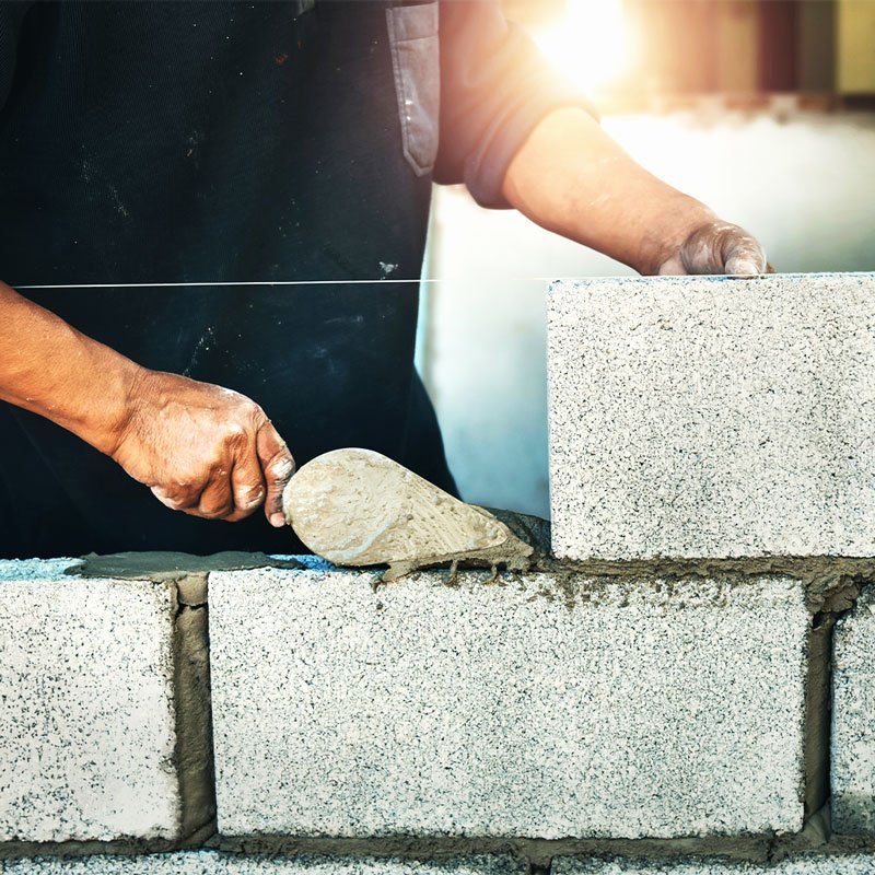 man in navy shirt building a grey  stone wall