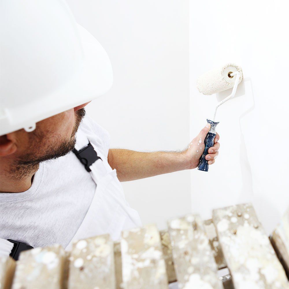 man in white helmet painting a white wall with a roller