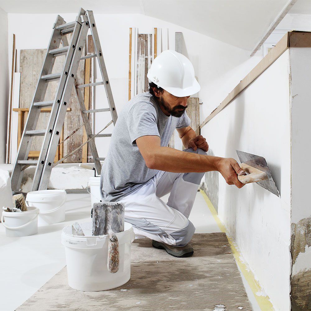 man in white helmet plastering a white wall