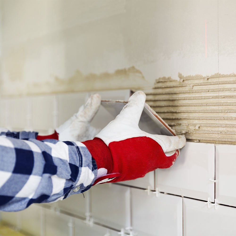 man in red gloves placing a ceramic wall tile