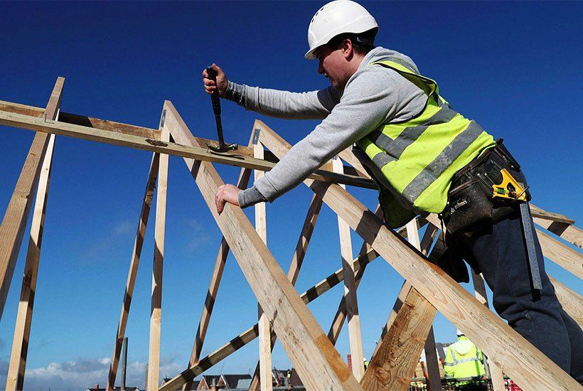 builder in white helmet removing a nail from a wooden plank