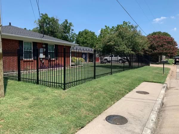 A black metal fence surrounds a brick house on a sunny day.