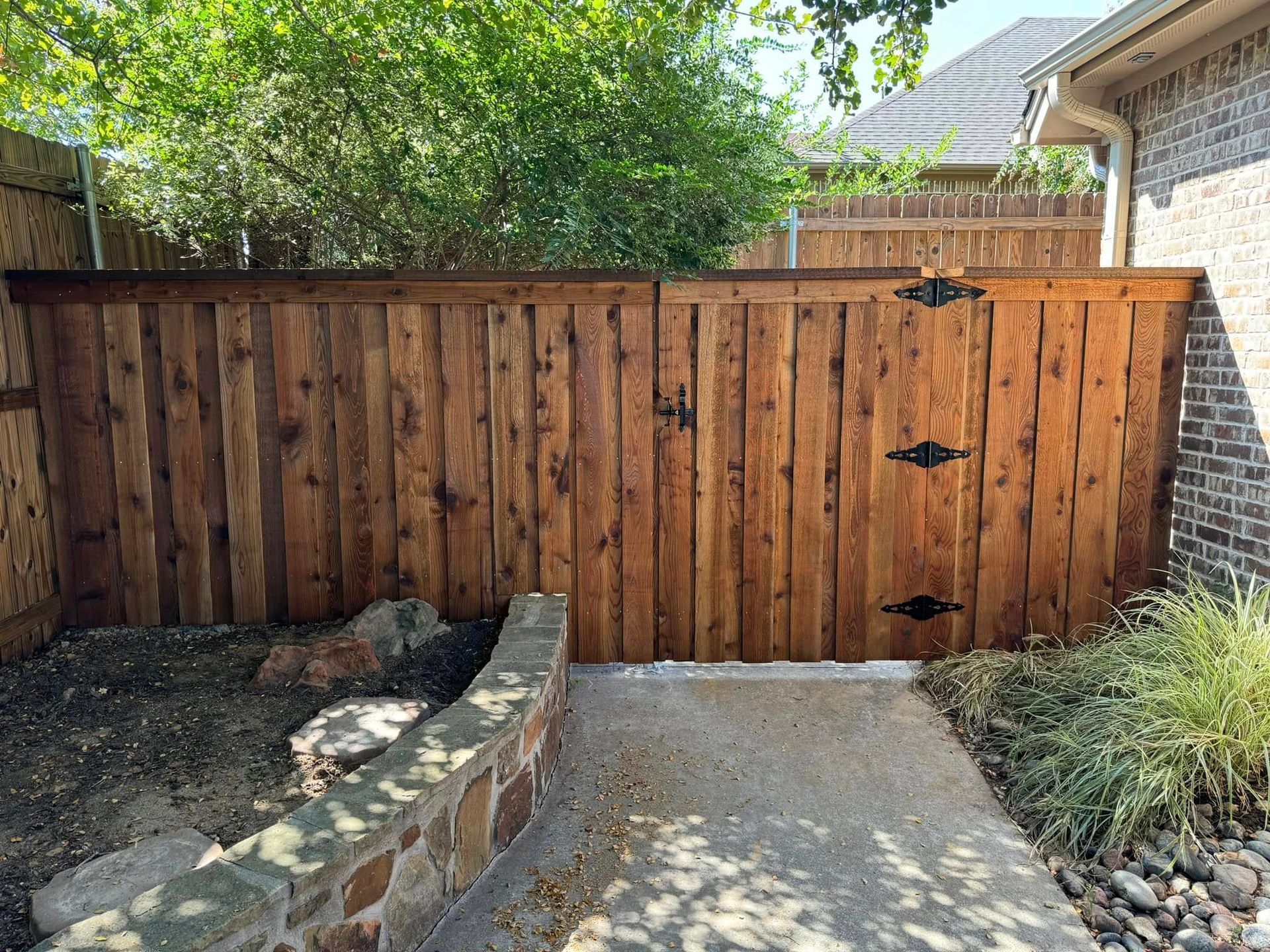 Wooden fence with double gate, brown stain, black hinges, and stone path entrance.