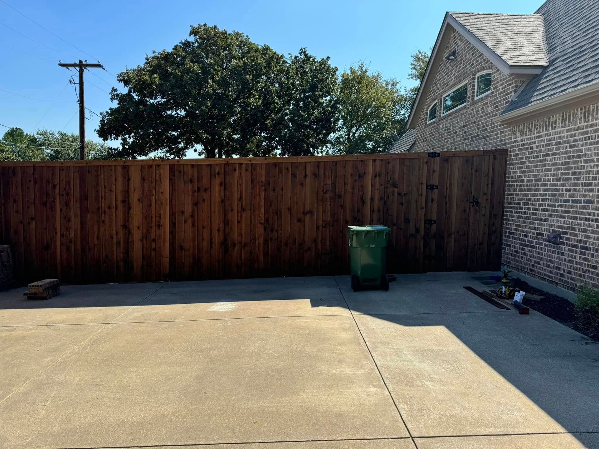 Backyard with brown wooden fence, concrete ground, and a green trash can.