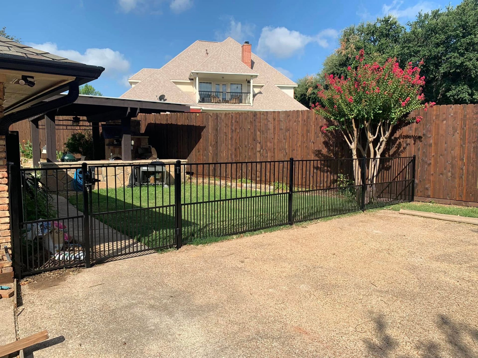 Black metal fence encloses a green lawn, gravel yard, and brown wooden fence in a backyard.