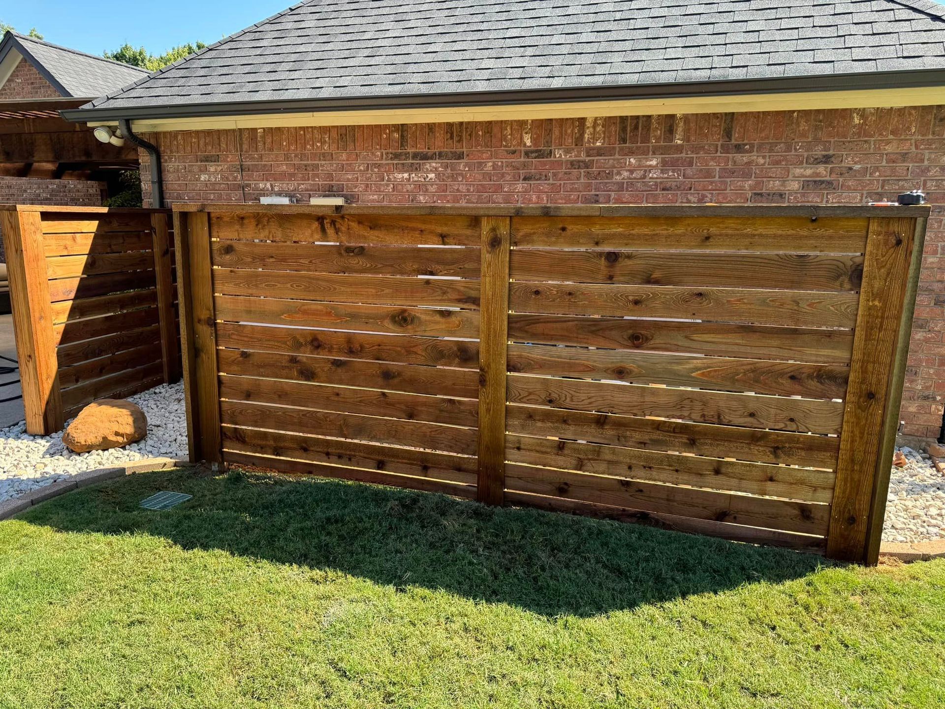 Wooden fence attached to a brick building with a grass lawn in front.