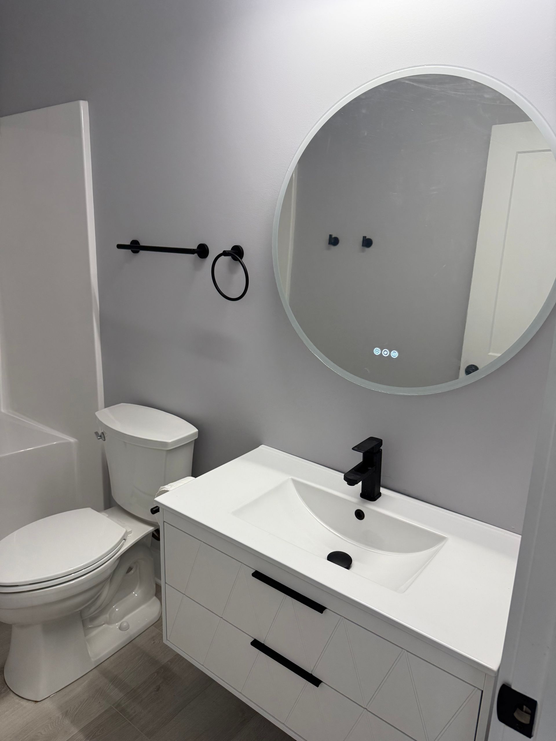 Modern bathroom with white vanity, round mirror, toilet, and gray walls