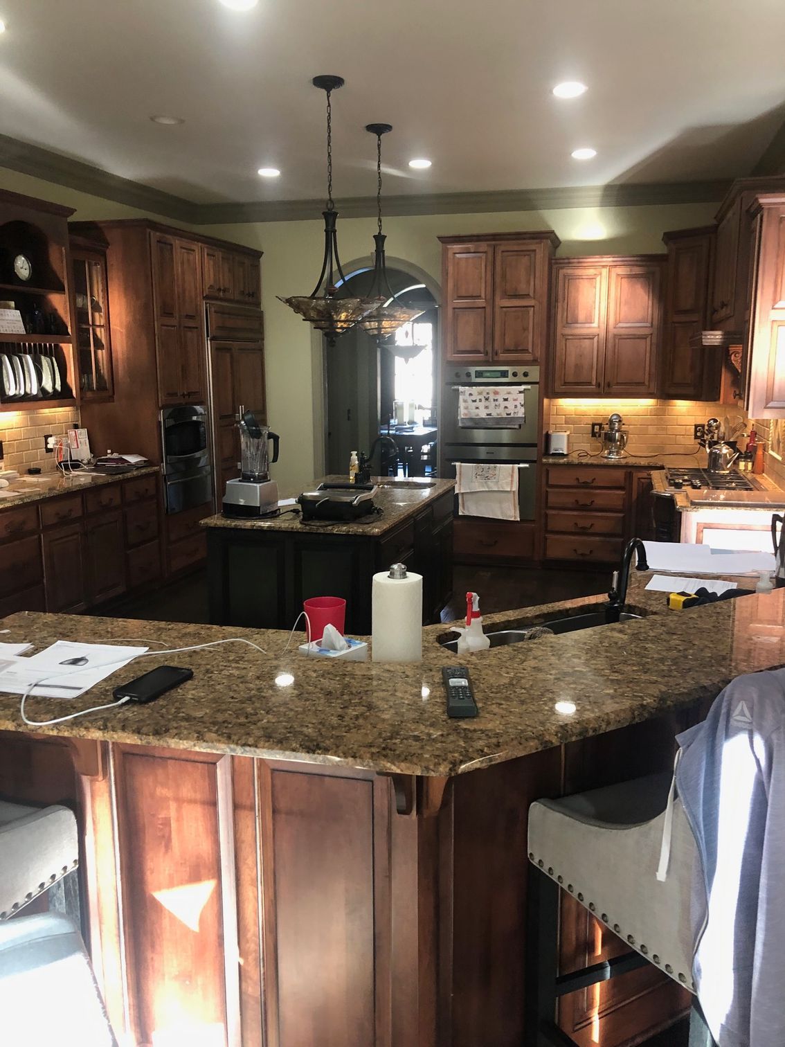 Warm kitchen with dark wood cabinets, granite island, pendant lights, and stainless appliances.