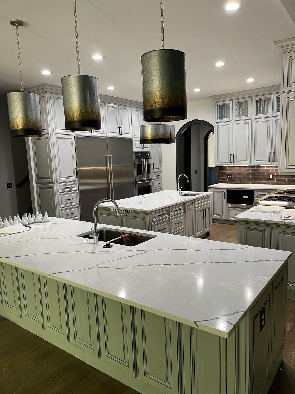 Modern kitchen with white marble island, stainless appliances, black pendant lights, and green lower cabinets