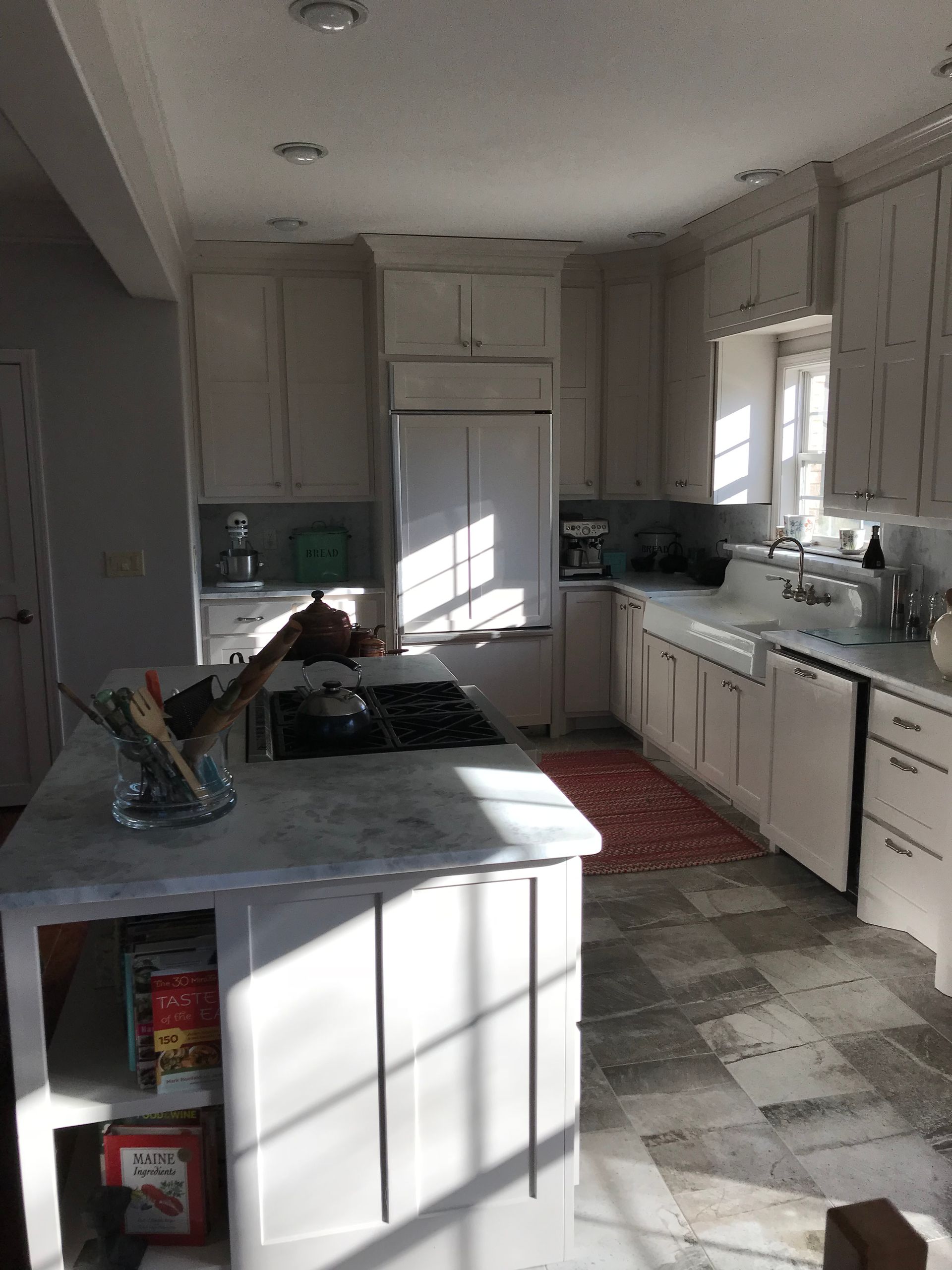 Bright white kitchen with central island, sink by window, and red rug on the floor.