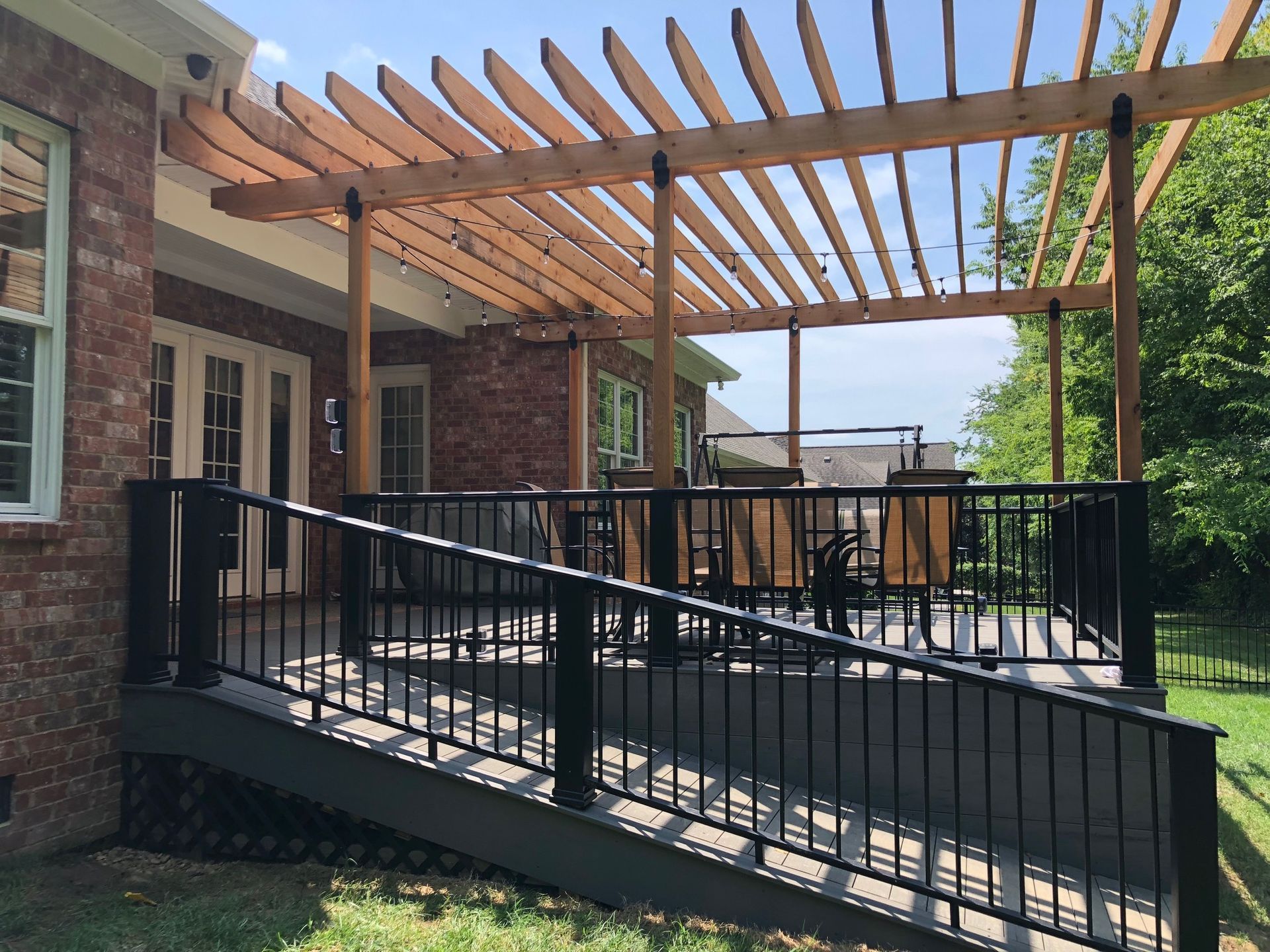 Brick patio ramp with black railings and wooden pergola beside a house