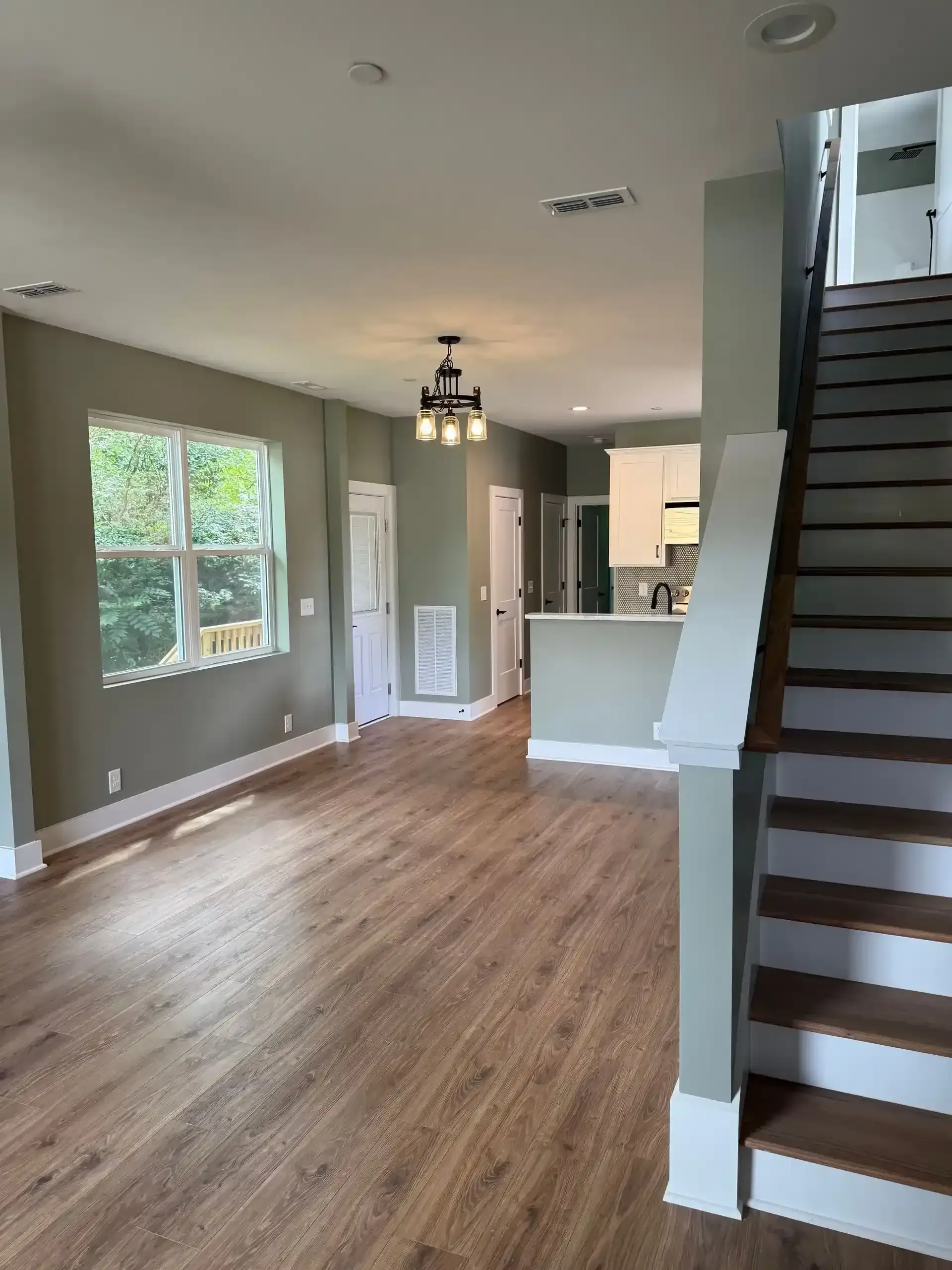 Empty open-plan living area with wood floors, gray walls, and a staircase on the right.