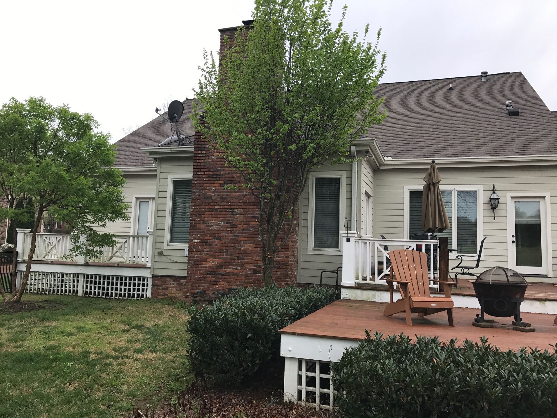 Suburban house patio with chairs, a grill, brick chimney, and trimmed hedges