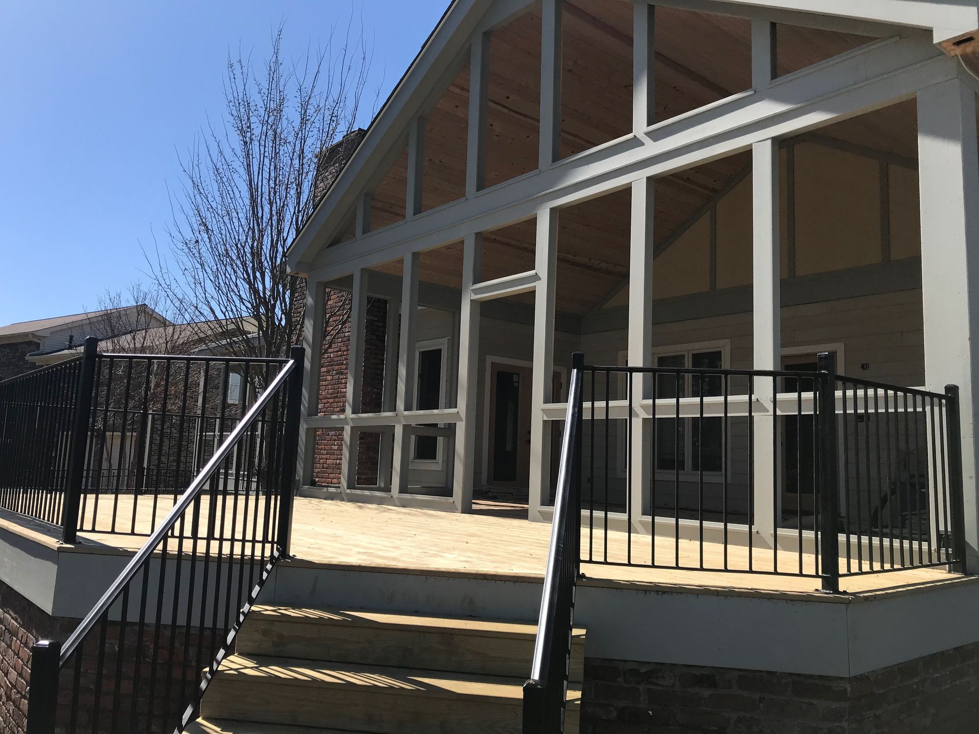 Modern house porch with large windows, black railings, and steps in bright sunlight