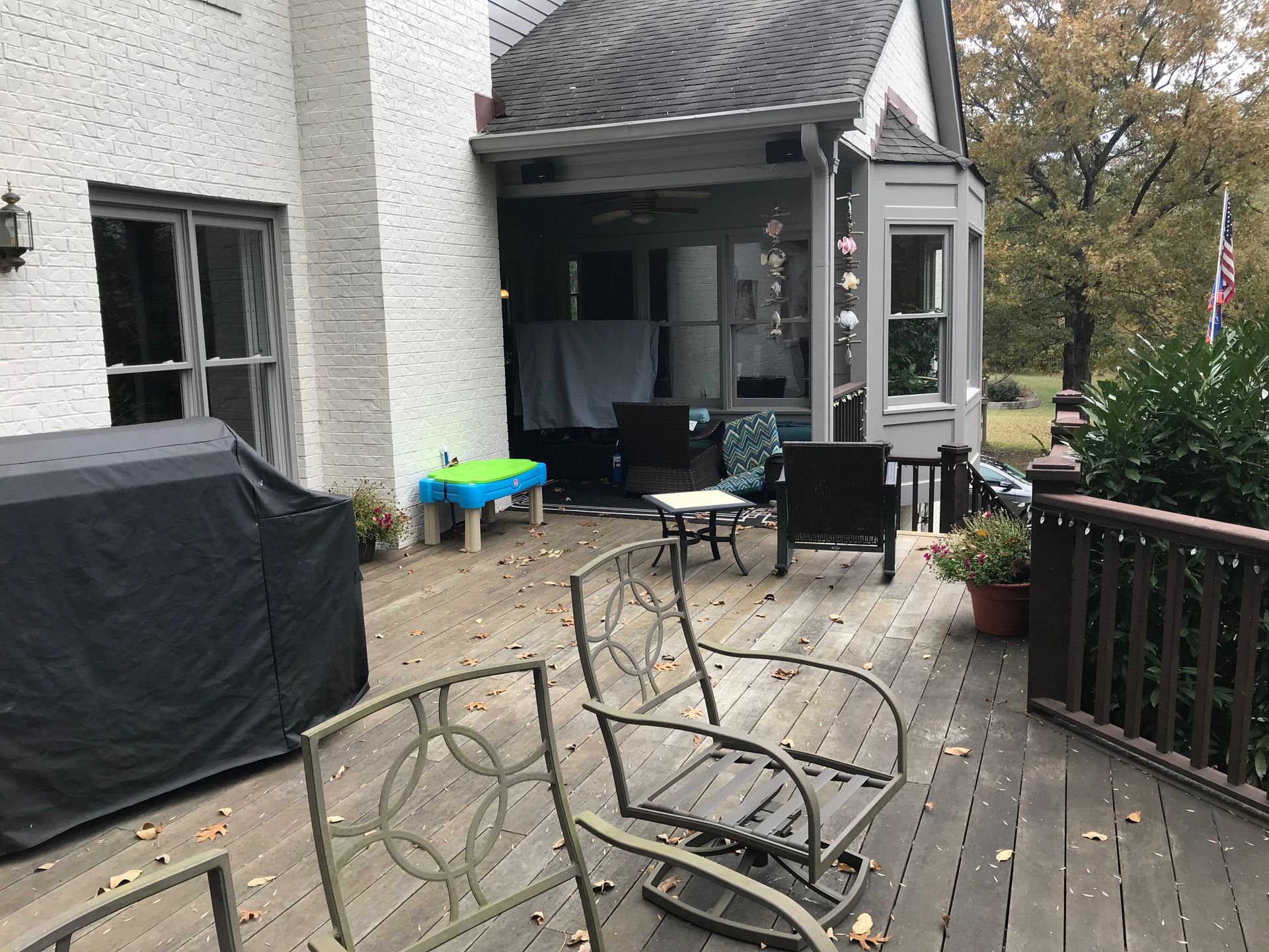 Patio deck with overturned metal chairs, covered grill, and house entrance in the background