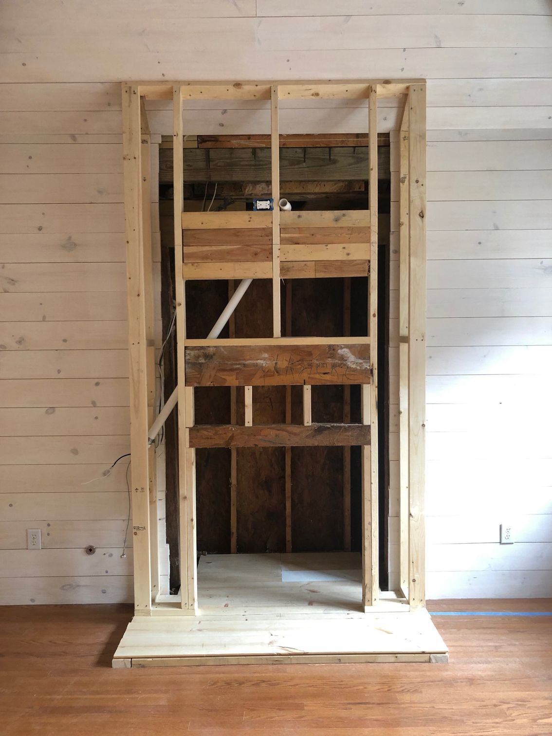 Framed wall opening with exposed wood studs and a small platform in a white-paneled room.