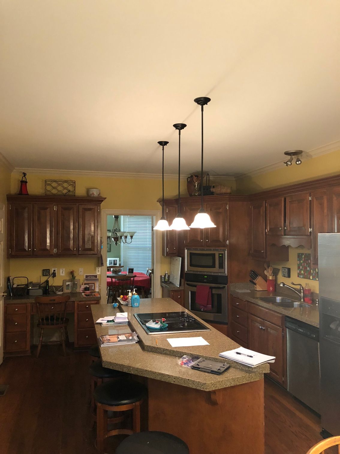 Warm-toned kitchen with wooden cabinets, granite island, hanging pendant lights, and a central sink.