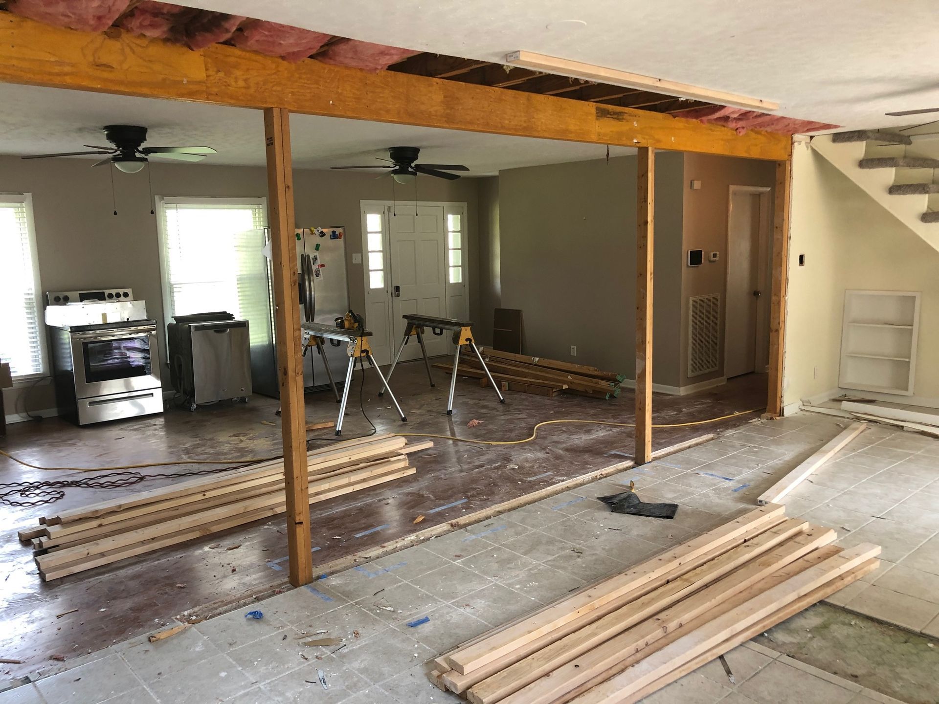 Renovation in progress inside a gutted room with exposed beams, tools, and stacked lumber on the floor