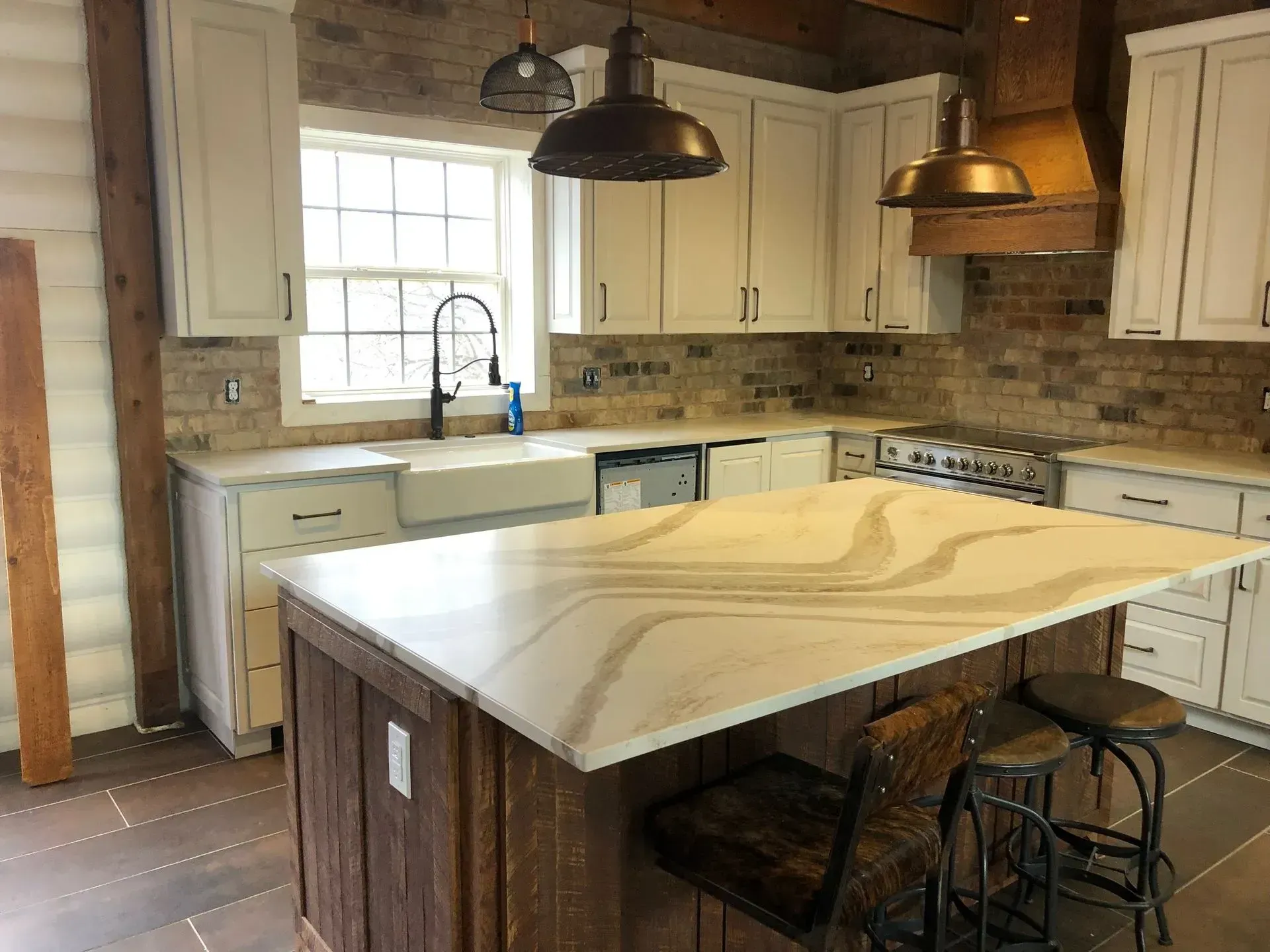Rustic kitchen with white cabinets, stone backsplash, large island, and dark pendant lights
