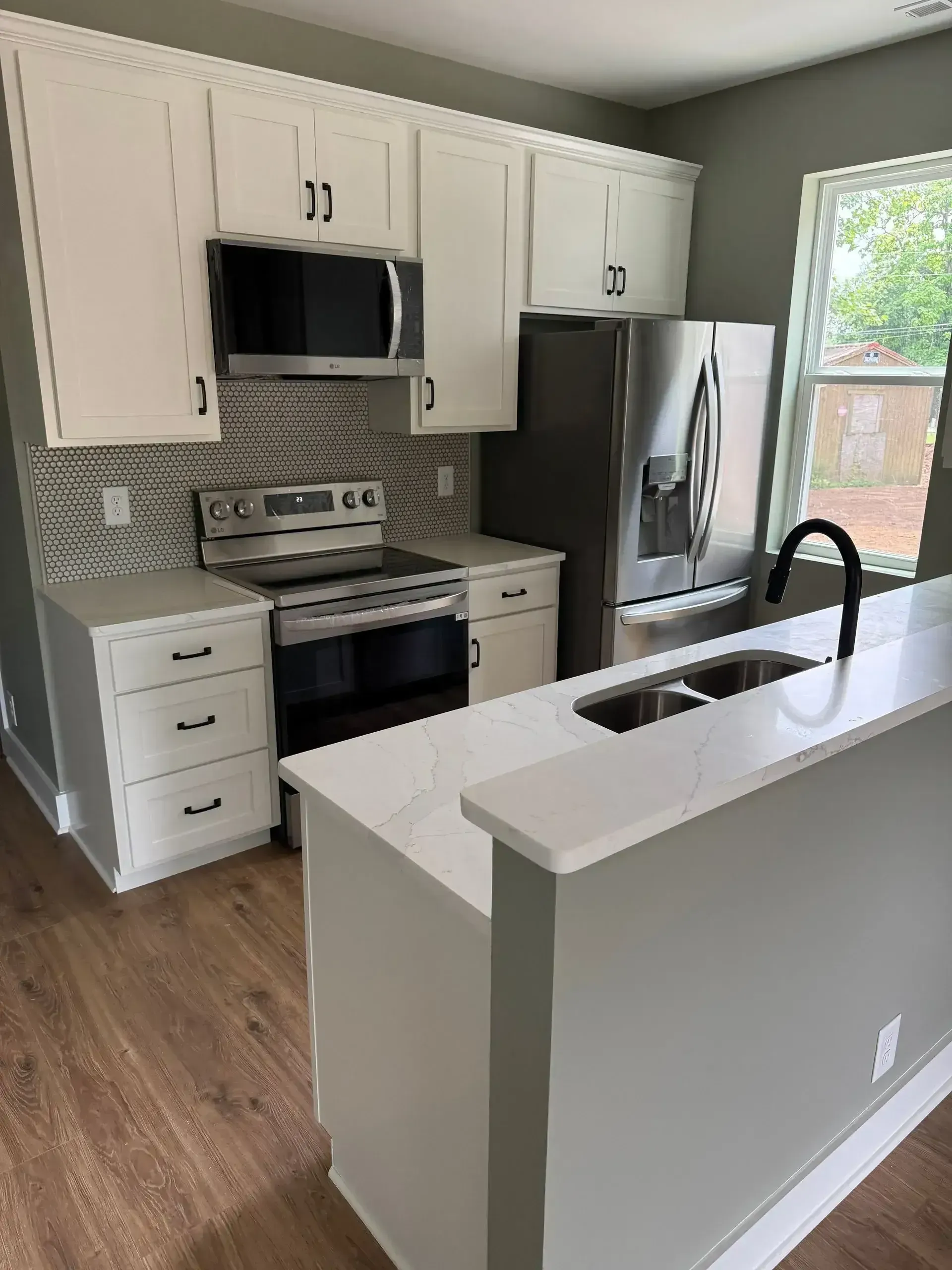 Bright white kitchen with stainless appliances, gray backsplash, wood floor, and a white island with black faucet