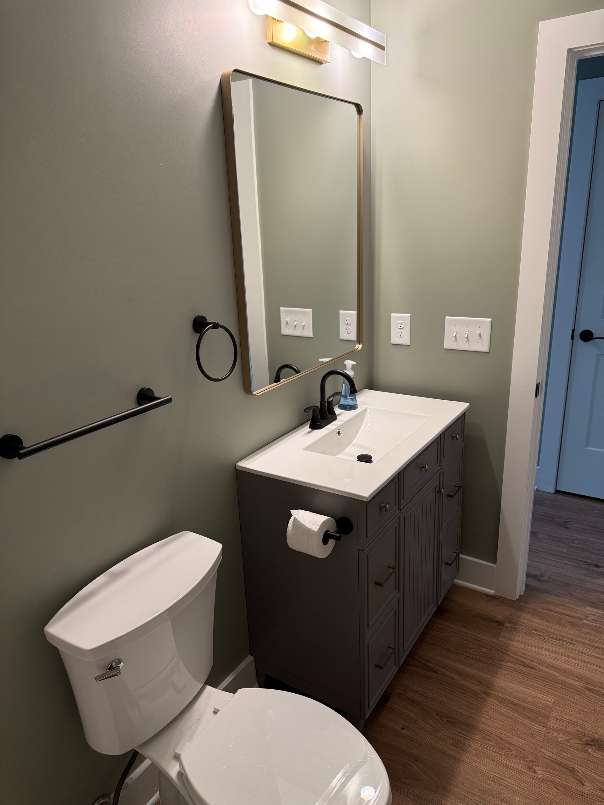 Small bathroom with toilet, vanity sink, mirror, and wood floor in gray tones