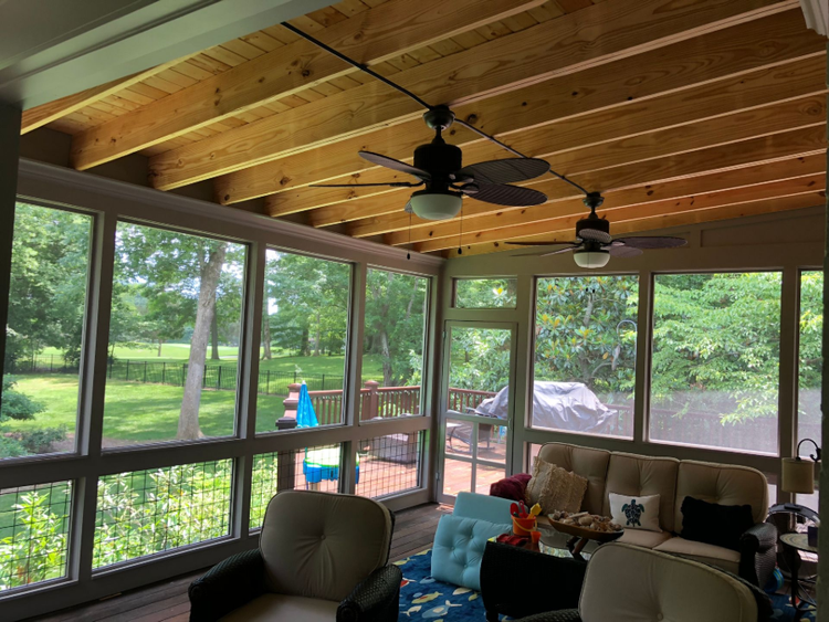 Screened porch with wood ceiling, ceiling fans, large windows, and outdoor seating overlooking a leafy yard