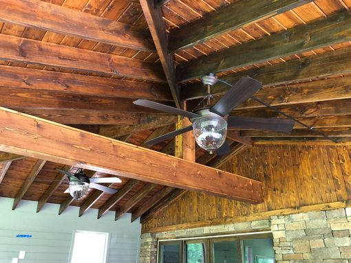Ceiling with exposed wooden beams and two ceiling fans in a rustic room
