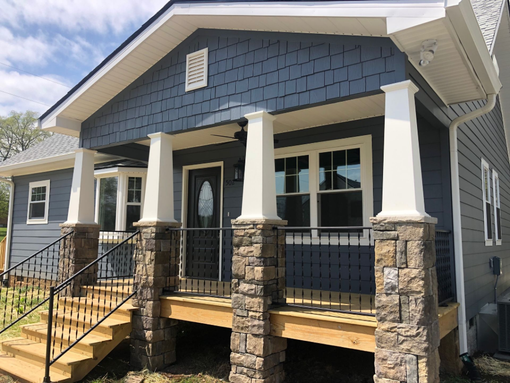 Blue house porch with stone columns, white trim, and black railing on a sunny day