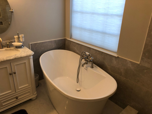 Modern bathroom with an oval freestanding tub, window blinds, and a vanity cabinet with sink.