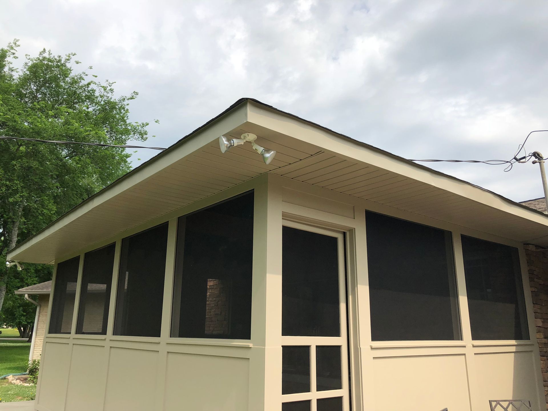 Small beige screened porch or gazebo with dark screens and a white door under a cloudy sky