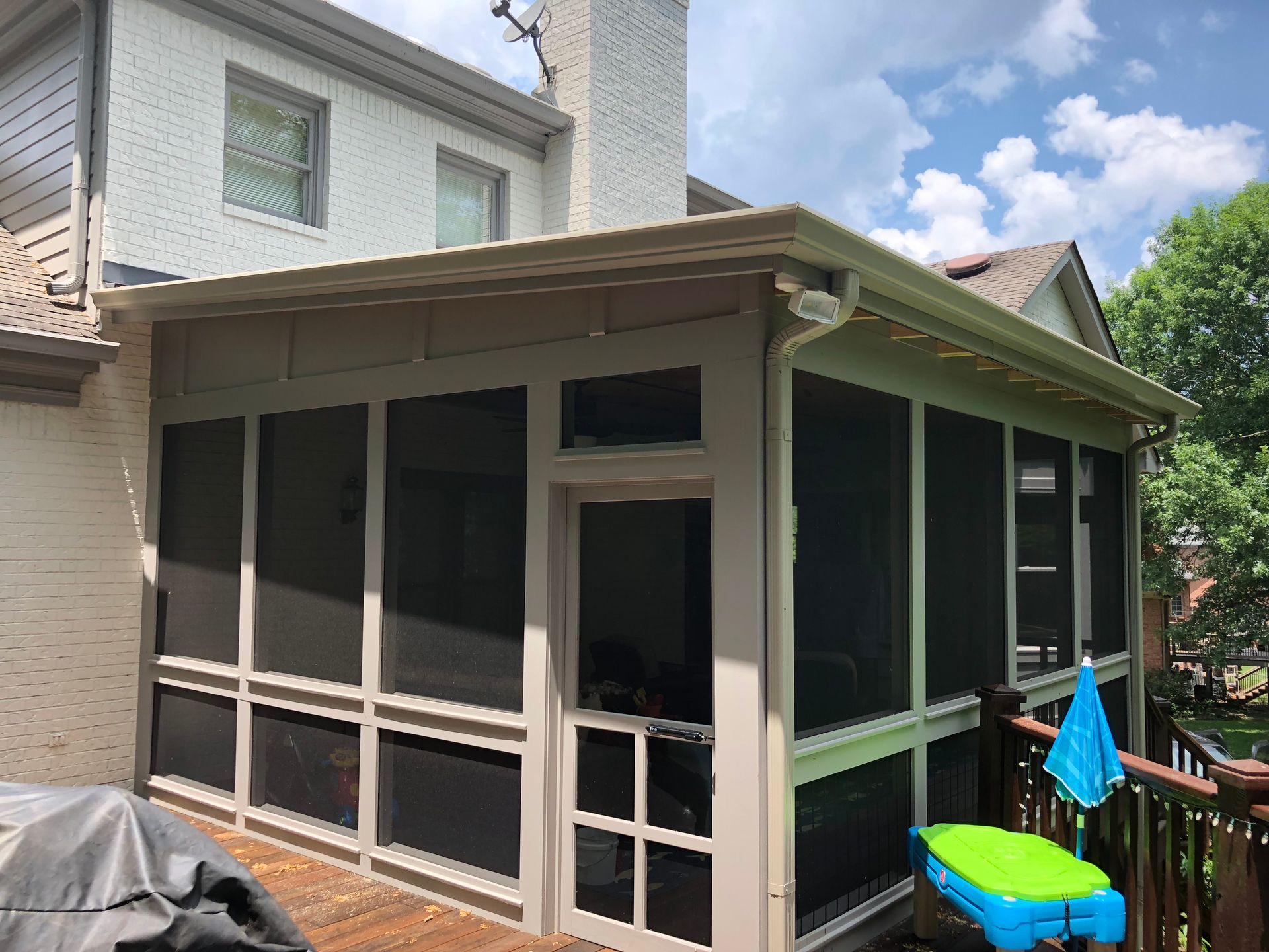 Screened backyard porch attached to a beige house, with black mesh panels and patio furniture nearby