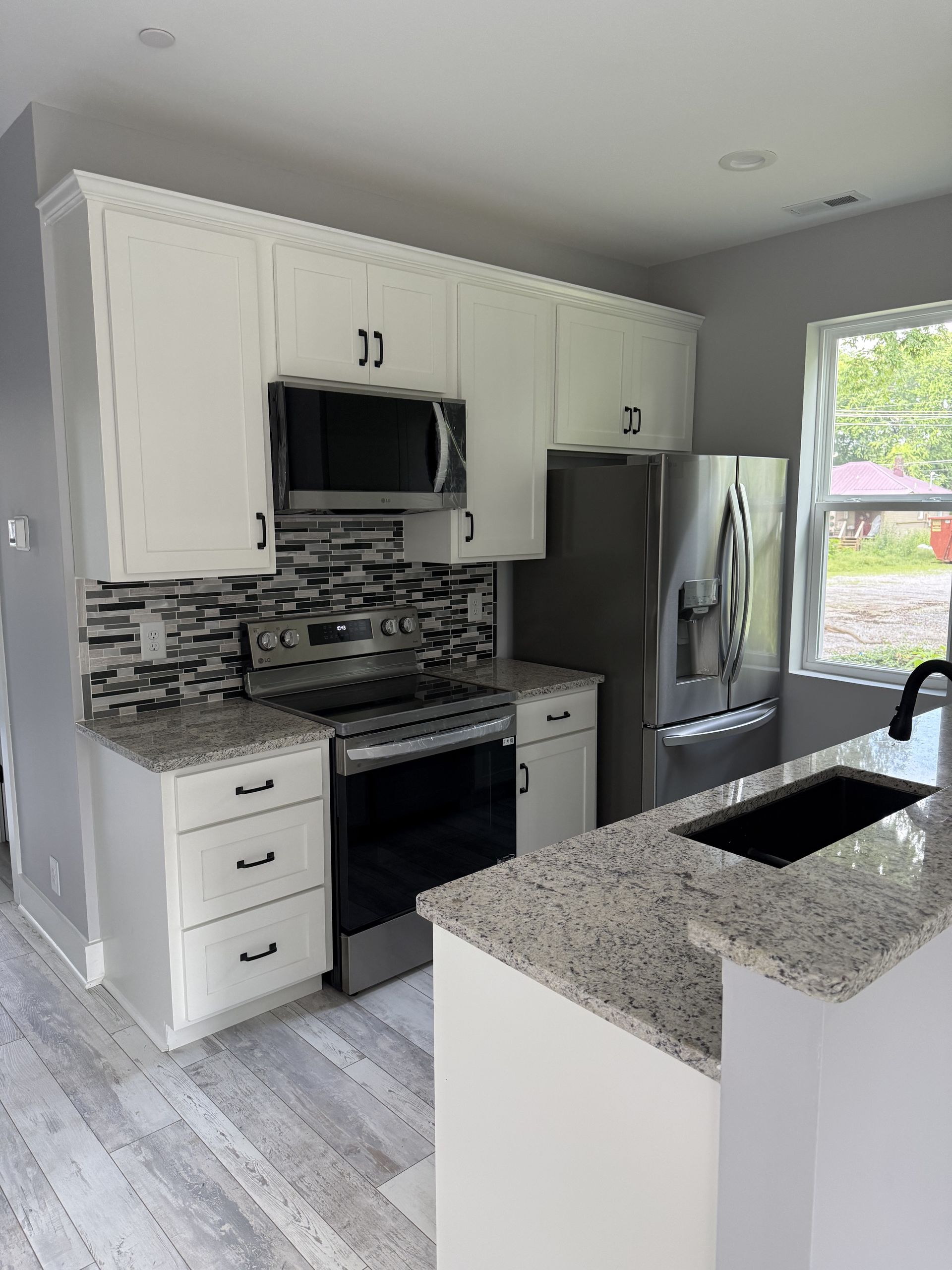 Bright modern kitchen with white cabinets, stainless appliances, and a gray granite island.